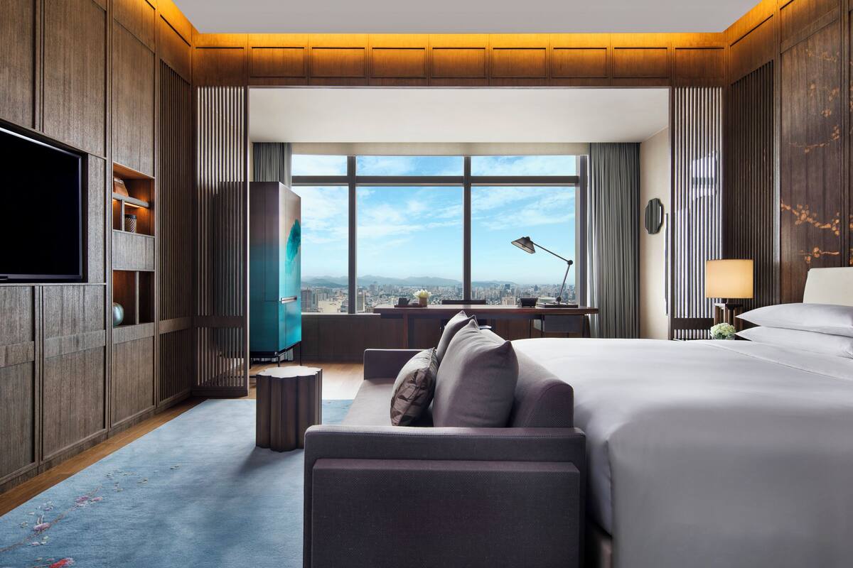 Habitació d'hotel moderna amb un llit gran, un escriptori, una televisió i vista a la ciutat.