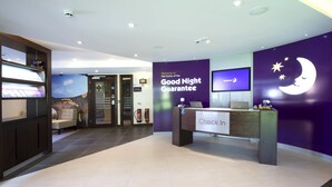 A hotel reception area with a 'Good Night Guarantee' sign, a reception desk, a television, and a wall with a moon and stars design. - Premier Inn Farnham (Farnham)