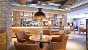 A bar area with a round table and leather chairs, a brick wall, and a wooden ceiling. - Premier Inn Farnham (Farnham)