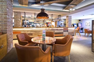 Zona de bar con una mesa redonda y sillones de cuero, pared de ladrillo y techo de madera.