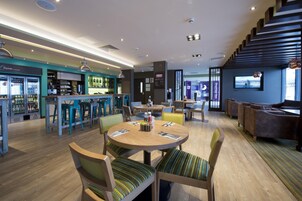Un moderno vestíbulo de hotel con una zona de bar, arreglos de asientos y una escalera.