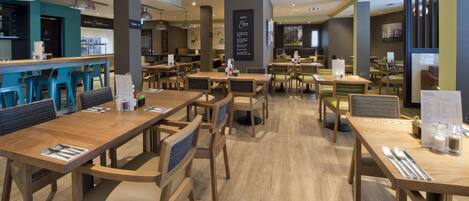 A spacious restaurant with multiple dining tables and chairs, a bar area, and a menu board.