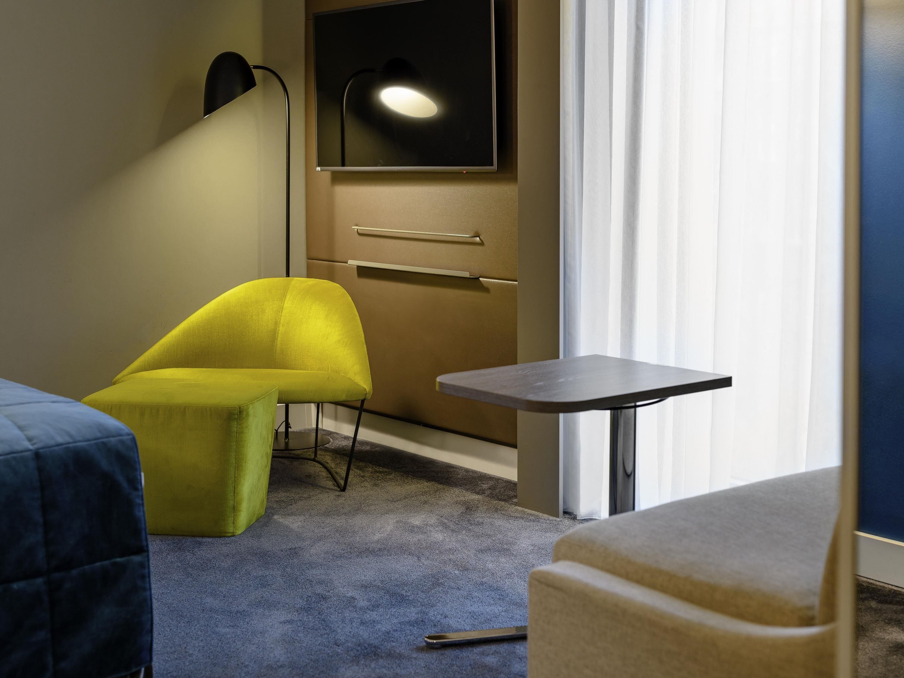 A room with a yellow armchair, a small table, a blue armchair, and a bed.