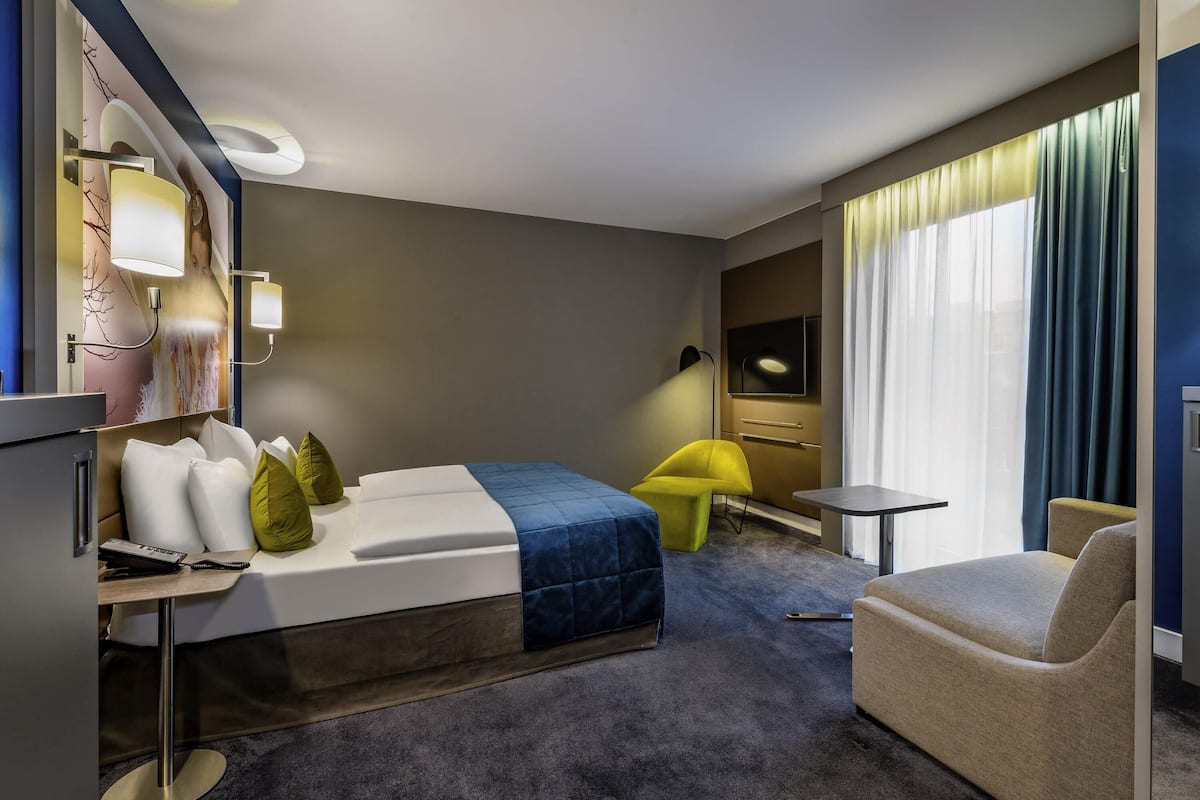 Ein modernes Hotelzimmer mit Bett, Schreibtisch, Stuhl und Fernseher.