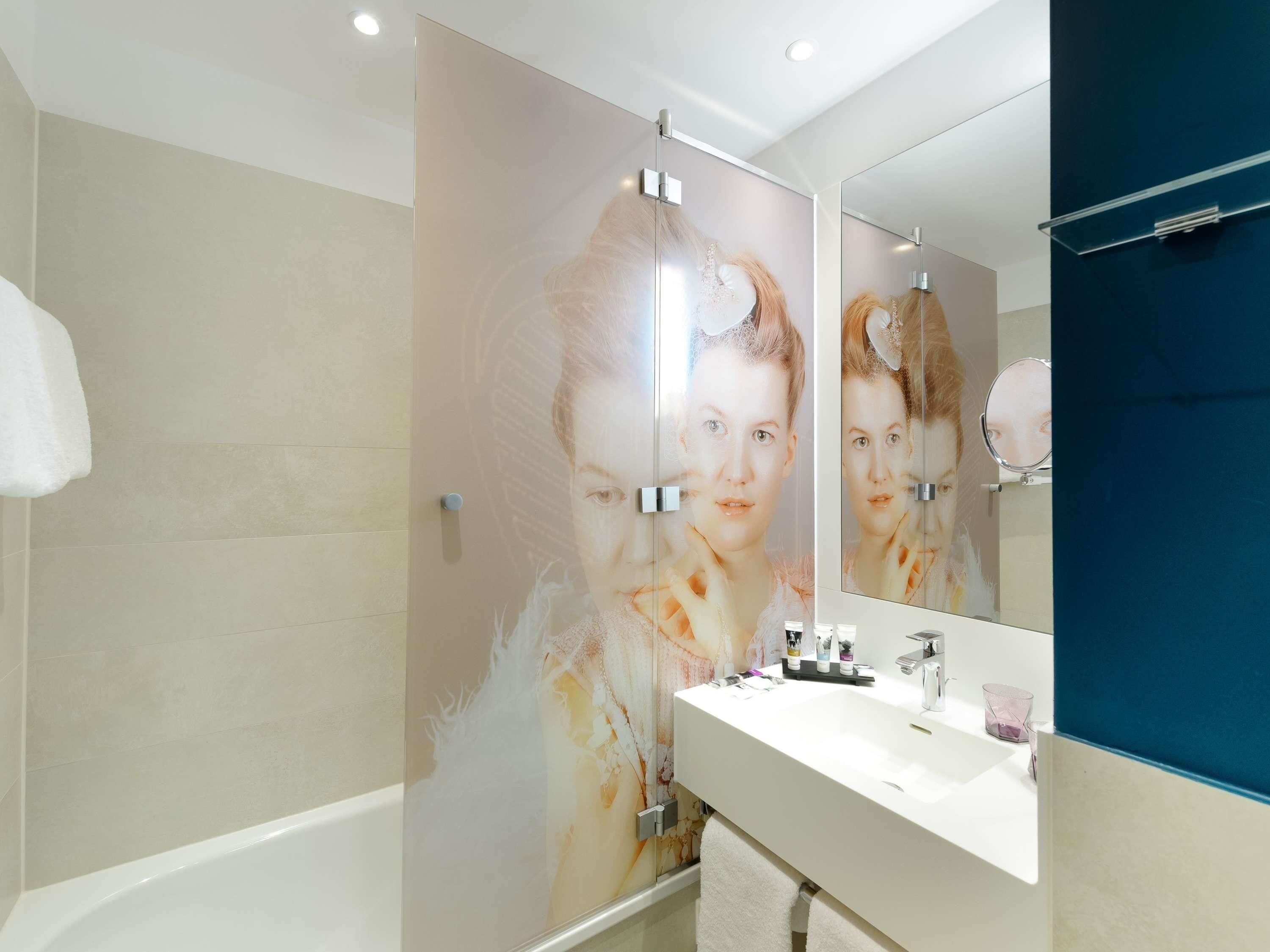 A modern bathroom with a large mirror, a bathtub, and a vanity with toiletries.