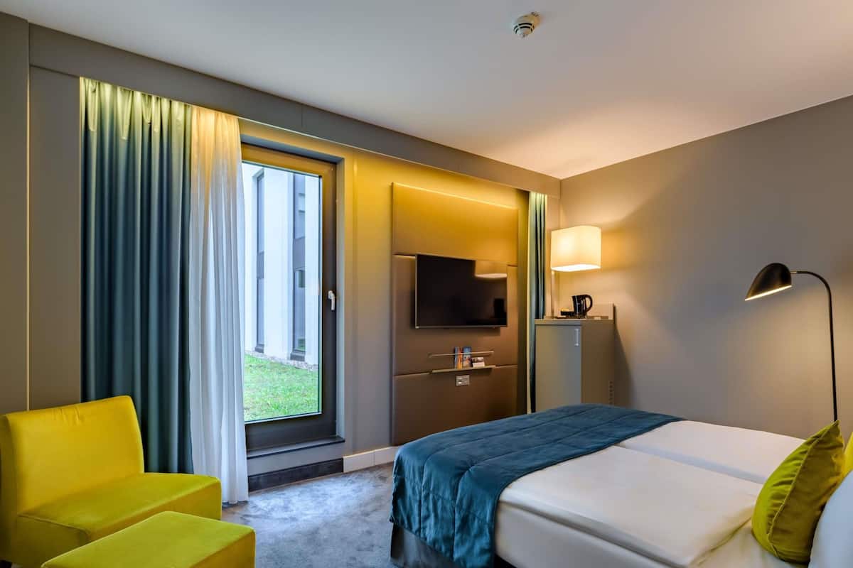 Ein Hotelzimmer mit Bett, Fernseher, Schreibtisch, Stuhl und einem fensterbepflegten Fenster.