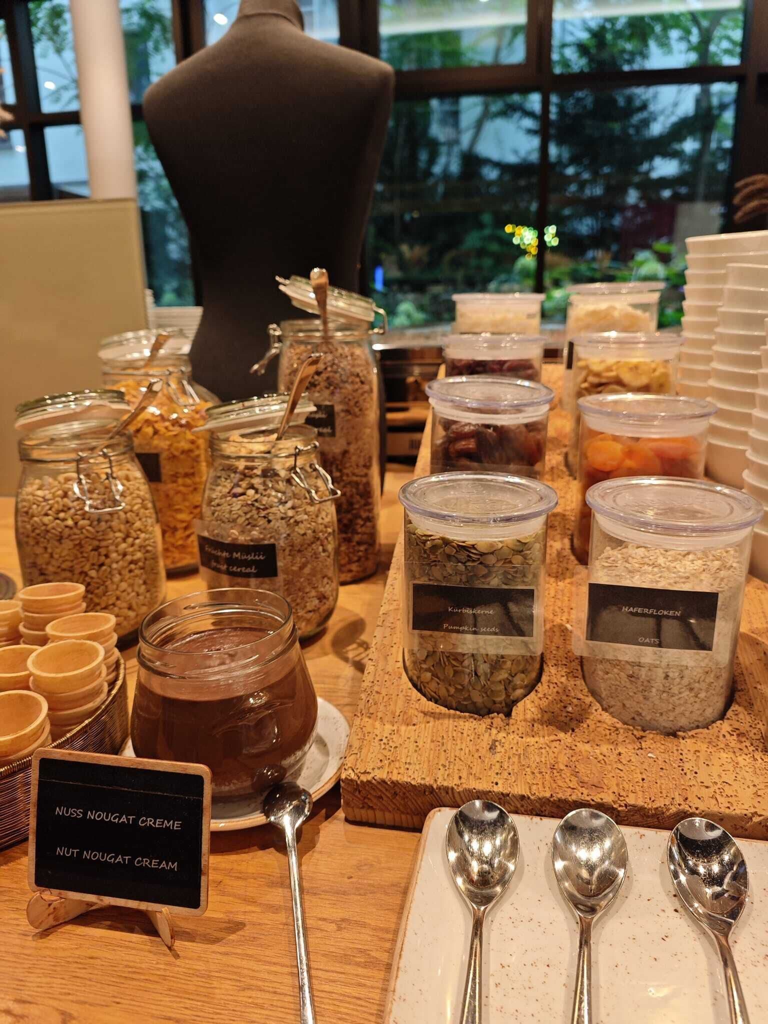 Exhibición de diversos alimentos, entre ellos botes de cereales, semillas y un letrero que indica 'Nuss Nougat Creme'.