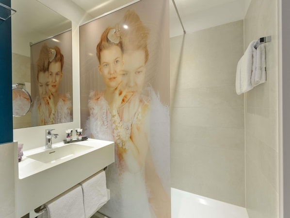 A bathroom with a large mirror, a sink, and a shower. - Mercure Hotel Berlin Wittenbergplatz (Berlin)