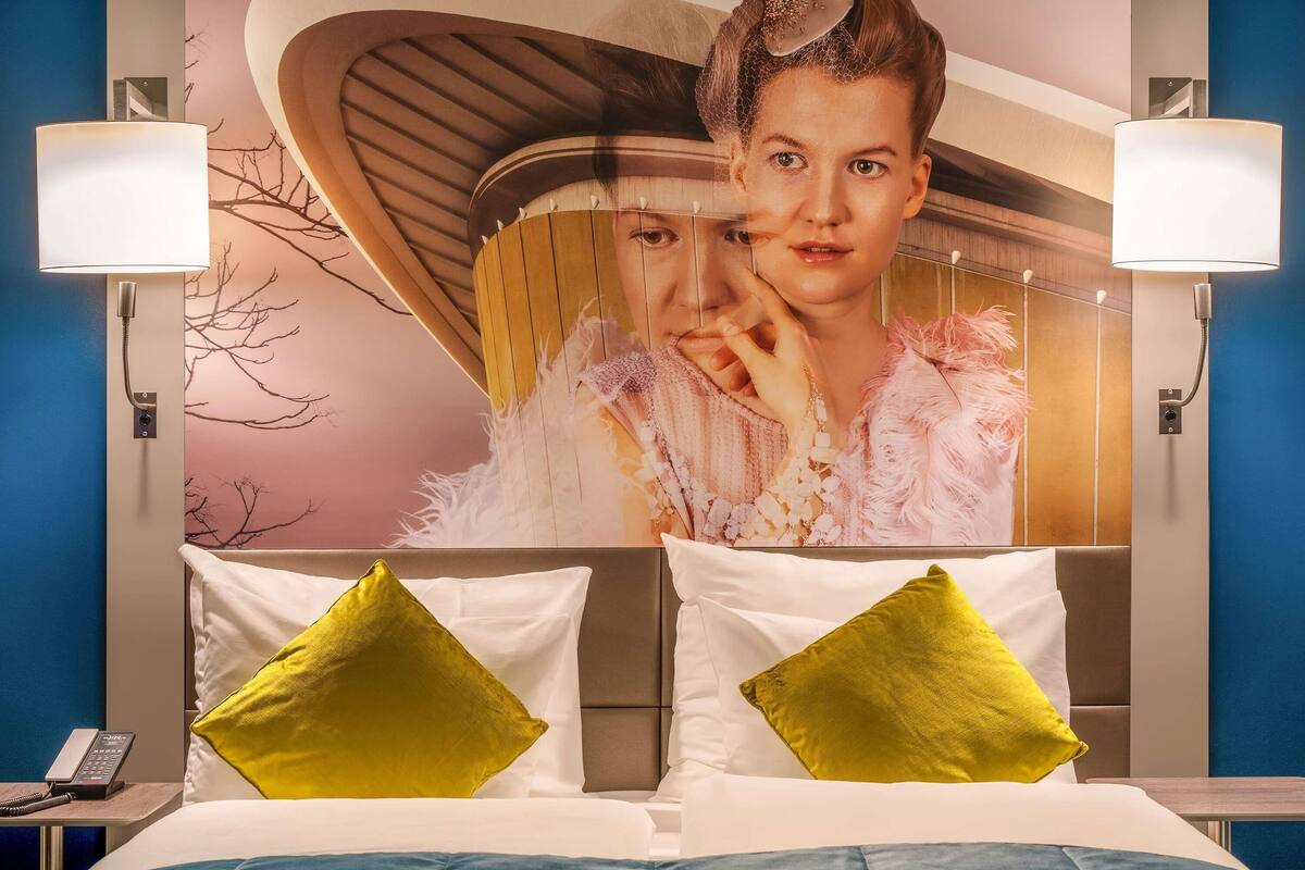 Ein Hotelzimmer mit einem Bett, zwei Kissen, einem Nachttisch mit Telefon und einem Wandposter.