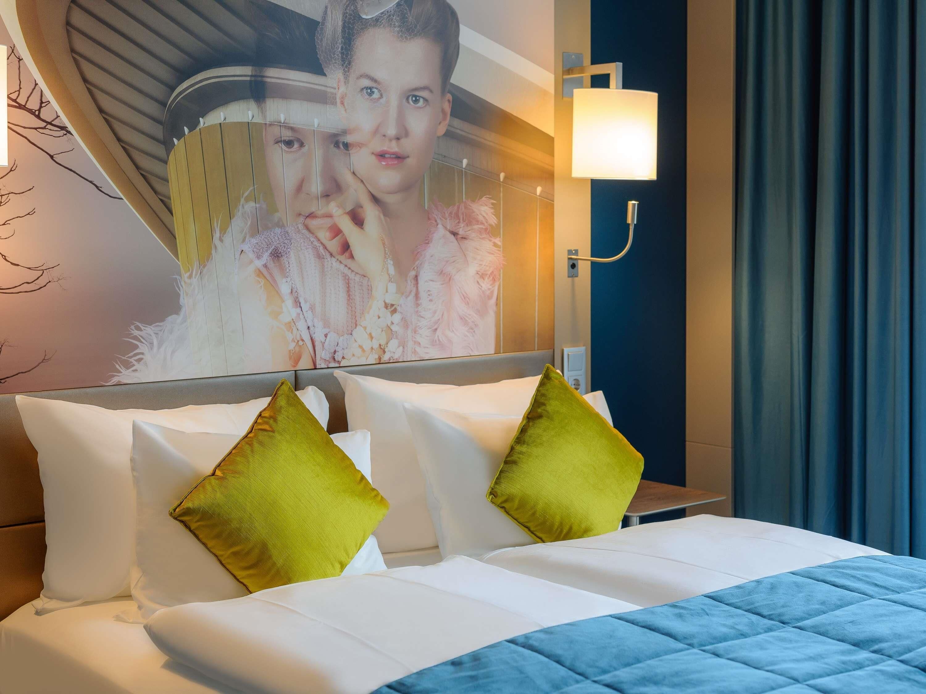 Une chambre d’hôtel avec un lit, des oreillers, une lampe fixée au mur et un tableau.