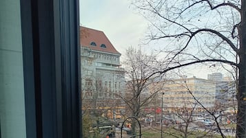 Vista desde el interior de un edificio, mostrando una calle con edificios, un árbol y algunas personas caminando.