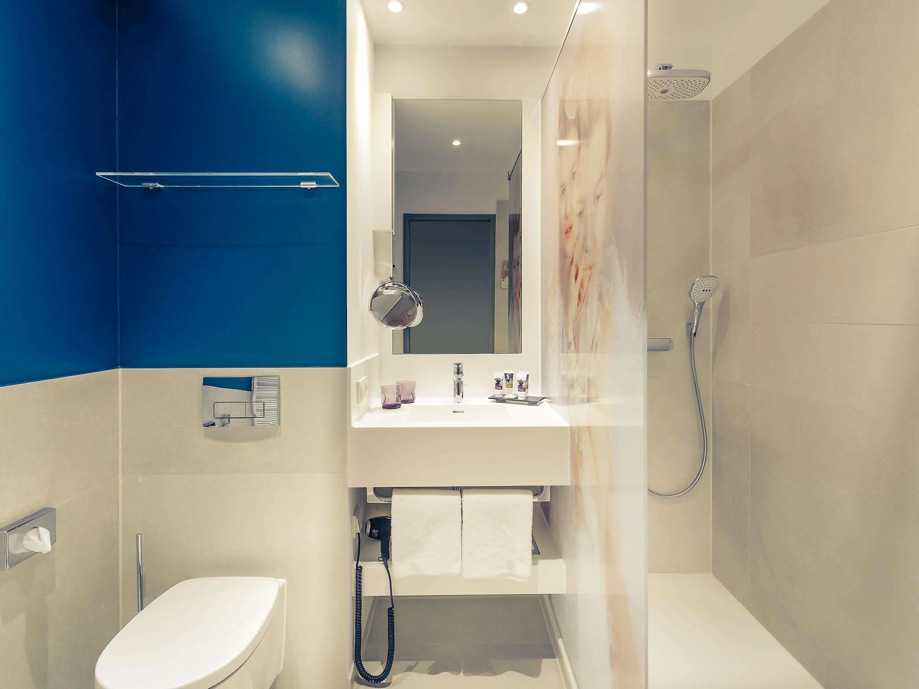 Ein modernes Badezimmer mit Waschbecken, Spiegel und Toilette. Eine Dusche mit Duschbrause und Handtuchhalter sind vorhanden.