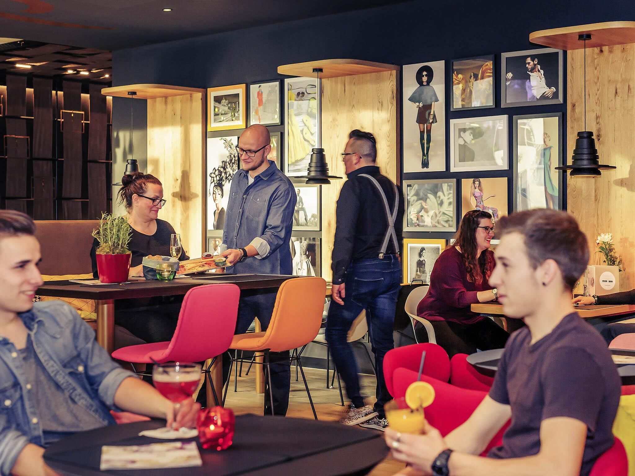 A modern restaurant interior with wooden accents, framed artwork on the walls, and a bar area.