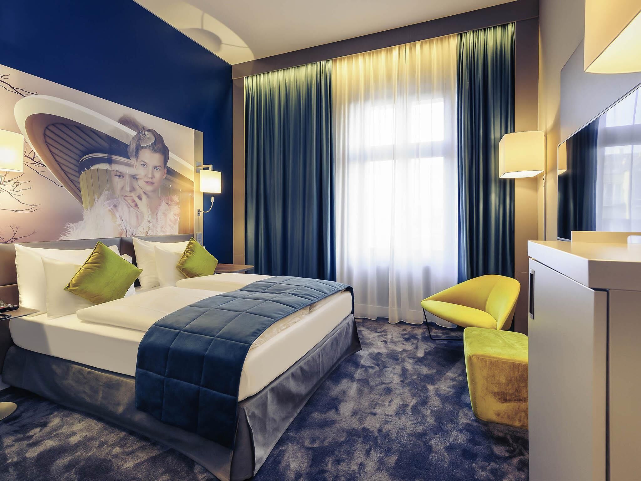 Een hotelkamer met een bed, een bureau, een stoel en een groot raam met gordijnen.