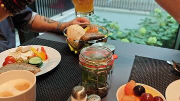 Ein Tisch mit einer Mahlzeit, darunter ein Salat-Teller, eine Schale mit Obst, ein Einmachglas mit Gurken und ein Glas Saft.
