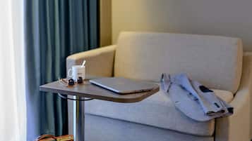 A hotel room with a sofa, a small table with a laptop, a cup, and a pair of sunglasses.