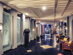 Un pasillo de hotel de diseño moderno, con un acceso central, zonas de estar y la entrada a un restaurante.