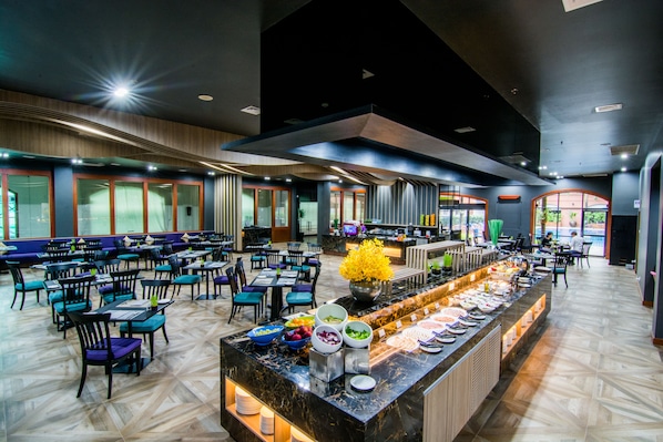 Ein geräumiges Restaurant mit mehreren Essplätzen, einem Buffet mit verschiedenen Speisen und großen Fenstern, die für natürliches Licht sorgen.