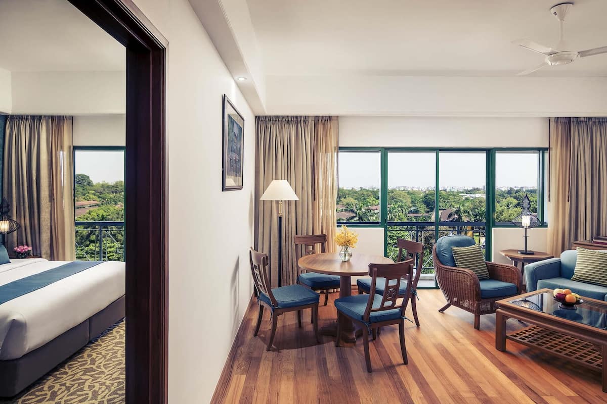 A hotel room with a bed, a dining table with chairs, a sofa, and a balcony with a view.