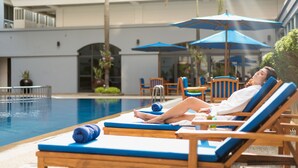 A poolside area with lounge chairs and umbrellas, a pool, and a building with balconies and windows. - Mercure Yangon Kaba Aye (Yangon)