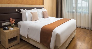 Una cama bien hecha con ropa de cama blanca y marrón, una mesita de noche con un teléfono y un jarrón de flores.