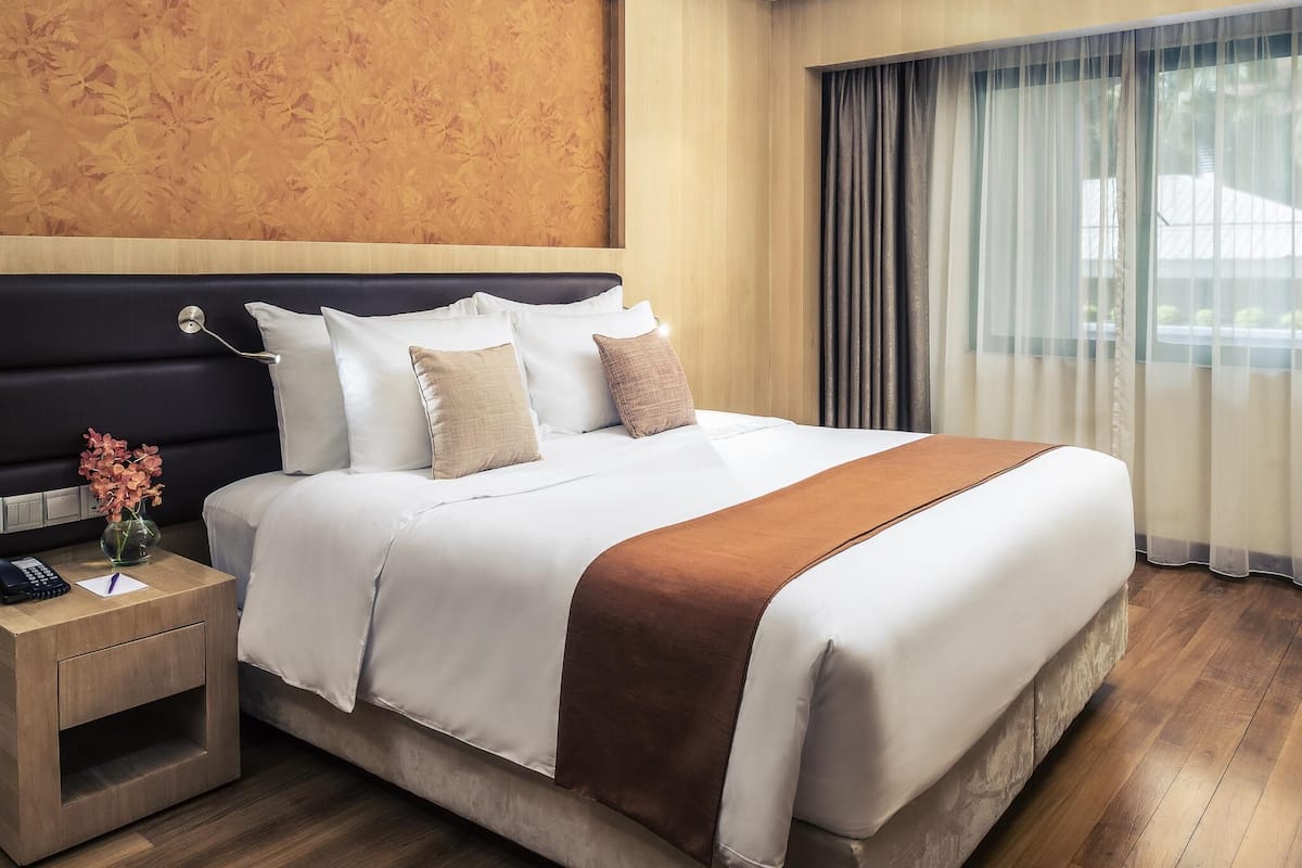 A hotel room with a large bed, a bedside table with a phone, and a nightstand with a vase of flowers.