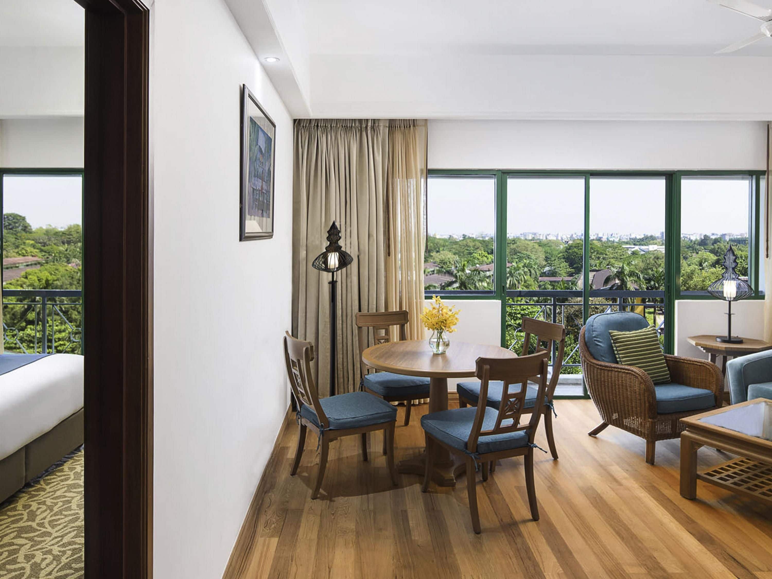 A room with a balcony, a dining table with chairs, a sofa, and a lamp.