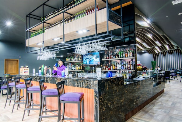 A bar area with multiple seating options, a bartender, and a variety of bottles and glasses.
