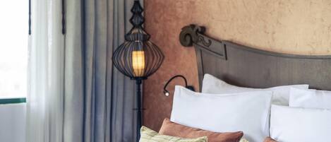 A neatly made bed with white and striped pillows, a headboard with a decorative design, and a wall-mounted lamp.