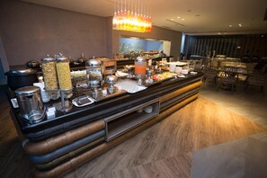 A buffet setup with various food items and containers, a coffee station, and seating arrangements. - Ibis Styles Batam Nagoya (Batam)