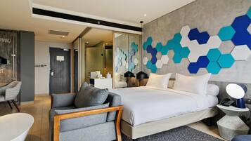 A modern hotel room with a large bed, a seating area with a chair, a small table, and a decorative wall.