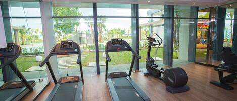 A modern gym with treadmills, a weight bench, and large windows offering views of a landscaped area.
