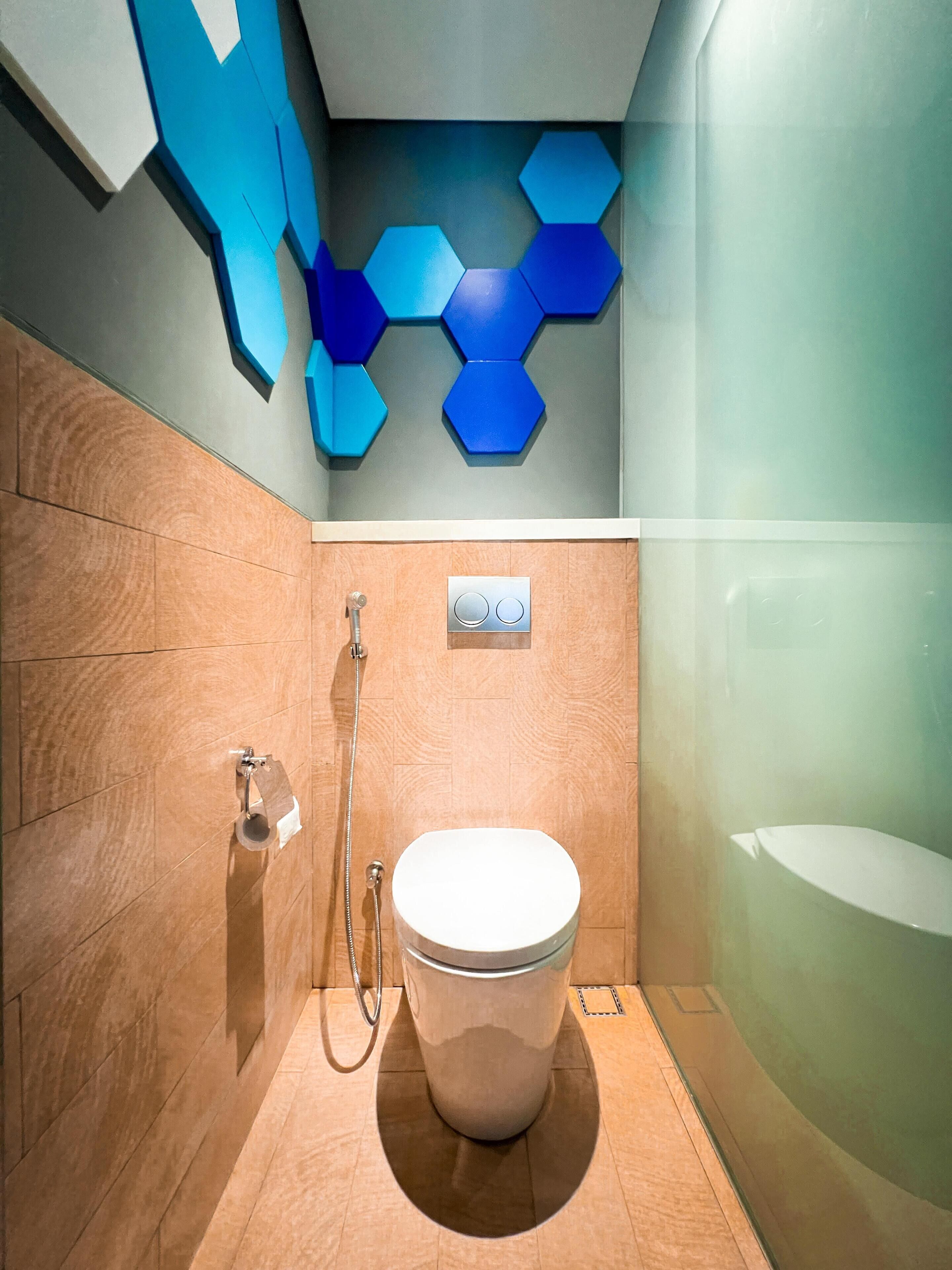 A modern bathroom with a wooden floor, a white toilet, a shower with a handheld showerhead, and a wall with blue hexagonal tiles.
