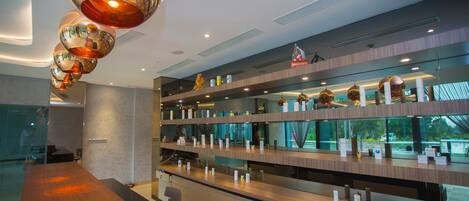 A modern hotel lobby with a long reception desk, multiple shelves with items, and a unique ceiling design with spherical mirrors.