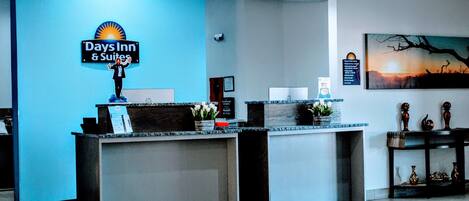 A reception desk with a 'Days Inn & Suites' sign, a framed certificate, and a painting of a sunset.