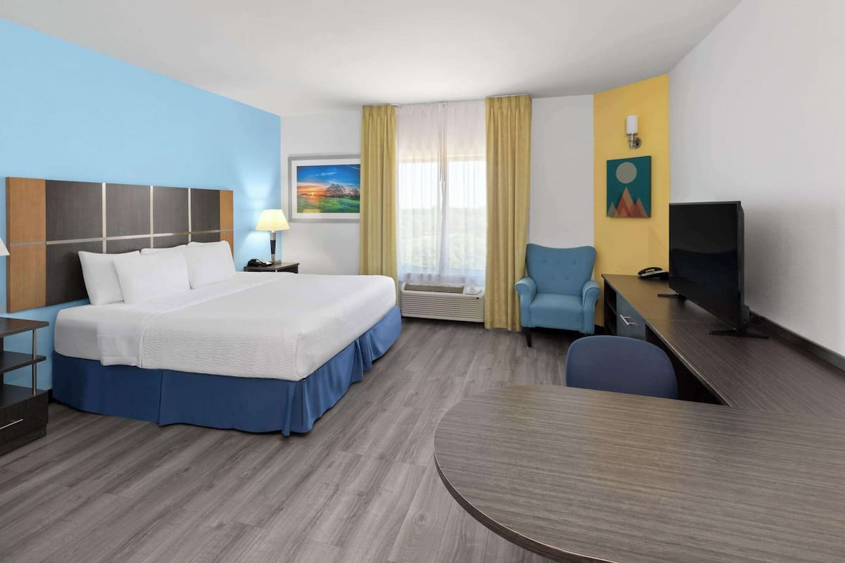 A hotel room with a large bed, a desk, a chair, a television, and a painting on the wall.