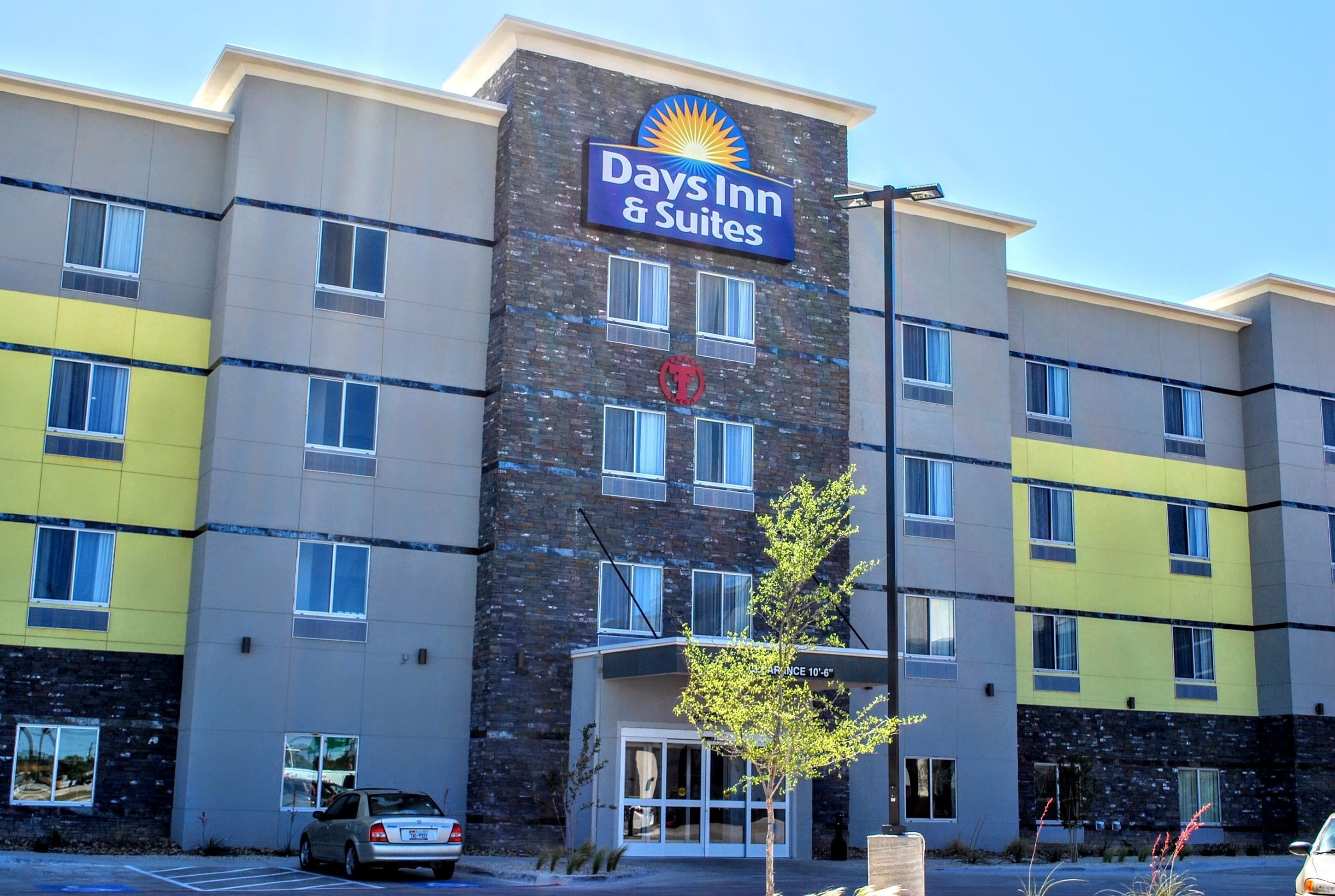 Ett hotell med flera våningar, med en skylt som visar att det är ett Days Inn & Suites. Hotellet har en modern design med en kombination av fasader i sten och målade fasader.