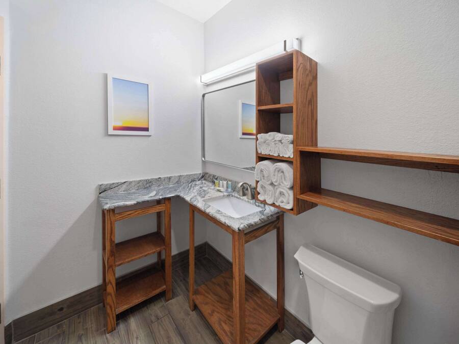 A bathroom with a wooden vanity, marble countertop, and a toilet.