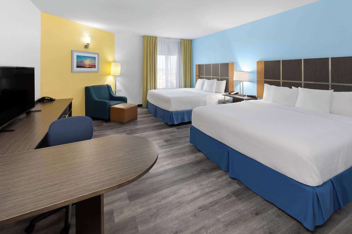 A hotel room with two beds, a desk, a chair, a TV, and a painting on the wall.