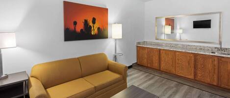 A modern hotel room with a sofa, a coffee table, a painting, a lamp, a mirror, and a wooden cabinet.