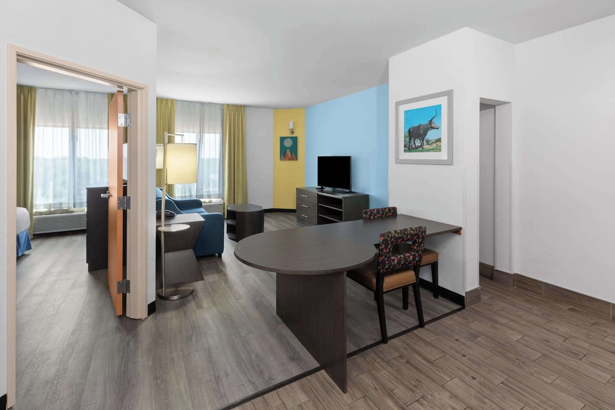 A modern hotel room with a dining area, a TV, and a painting on the wall.