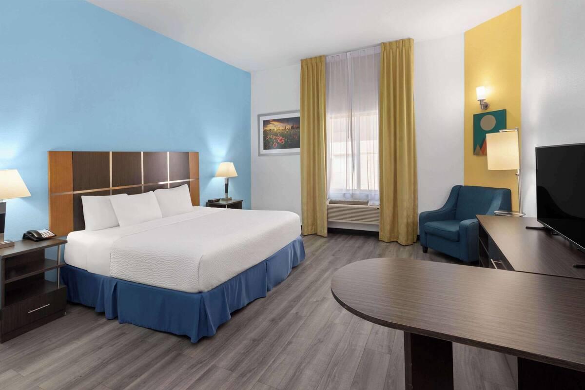 A hotel room with a large bed, bedside tables, a desk, a chair, a television, and a window with curtains.
