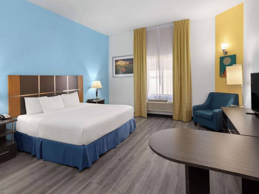 Habitación de hotel con una cama grande, mesitas de noche, un escritorio, una silla, un televisor y una ventana con cortinas.