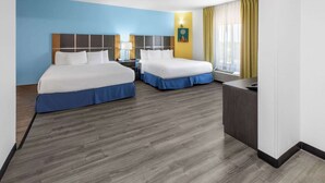 A hotel room with two beds, a desk, a nightstand, and a window with curtains.