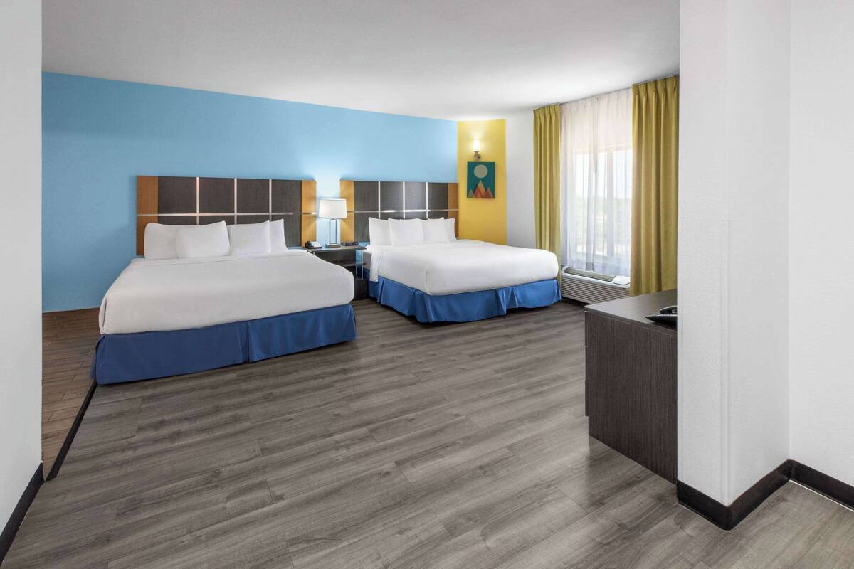 A hotel room with two beds, a desk, a nightstand, and a window with curtains.