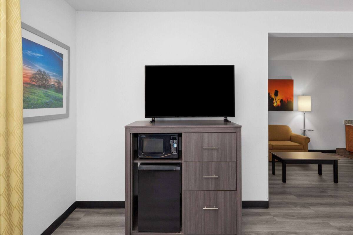 A compact kitchenette with a microwave, a small refrigerator, and a flat-screen TV on a cabinet.