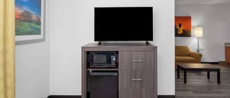 A compact kitchenette with a microwave, a small refrigerator, and a flat-screen TV on a cabinet.