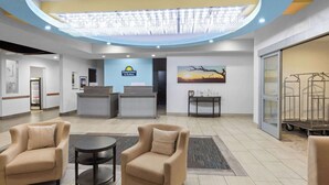 A hotel reception area with a reception desk, two armchairs, a small table, and a chandelier.