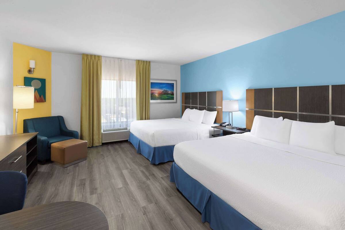 A hotel room with two beds, a desk, a chair, a lamp, and a window with curtains.