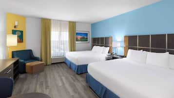 A hotel room with two beds, a desk, a chair, a lamp, and a window with curtains.